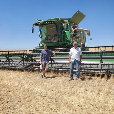 Two men standing in front of a combine harvester in a wheat field